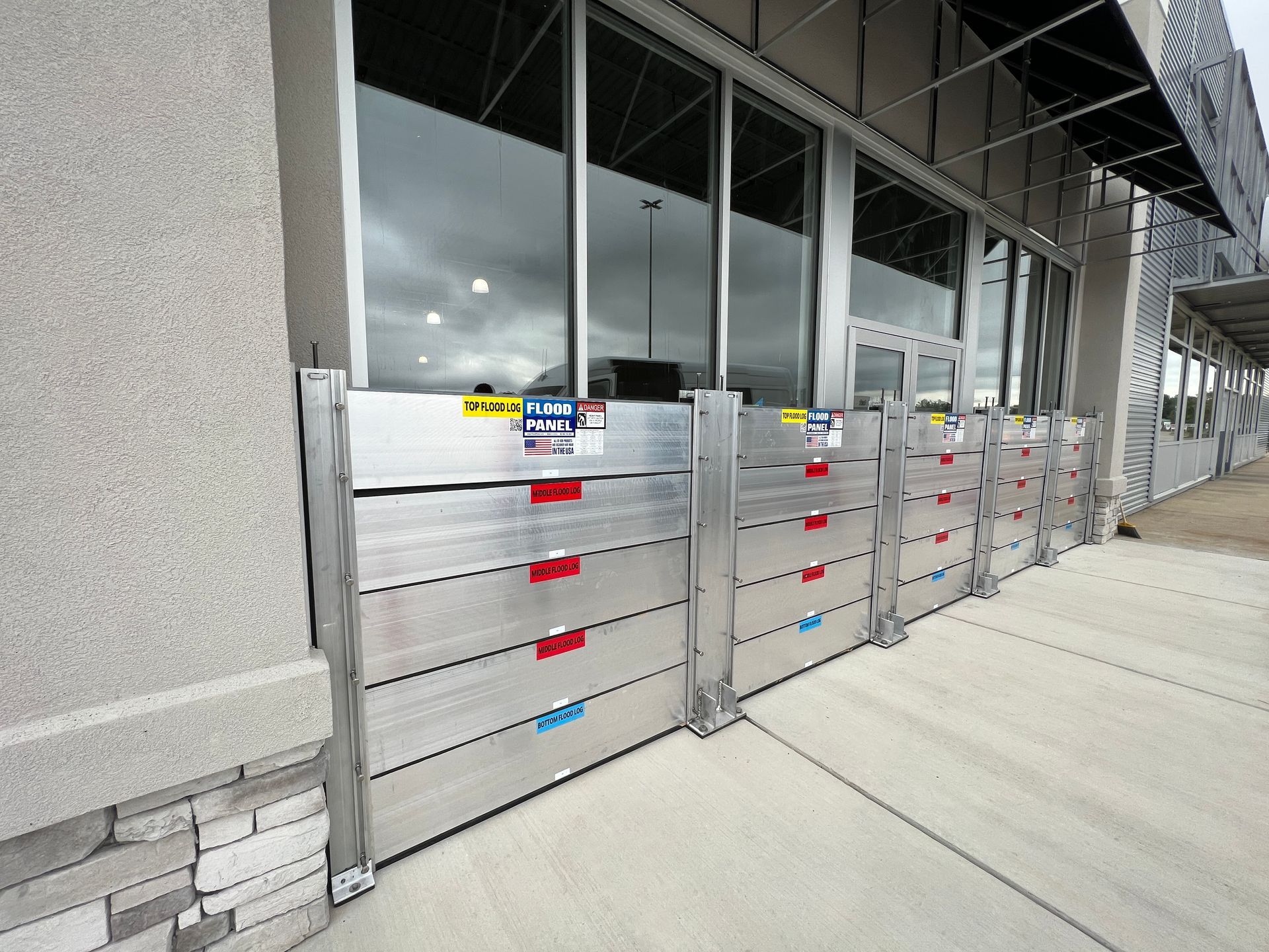 A row of aluminum flood barriers on the sidewalk in front of a building.