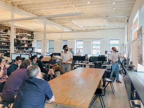 A group of people are sitting around a long wooden table in an office.