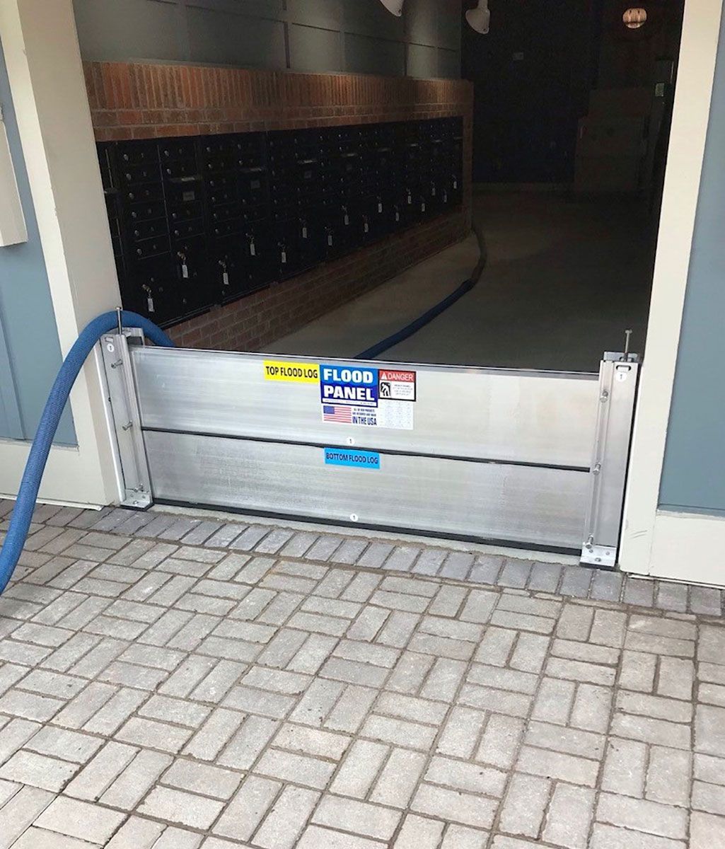 A hose is attached to a flood barrier in front of a building.