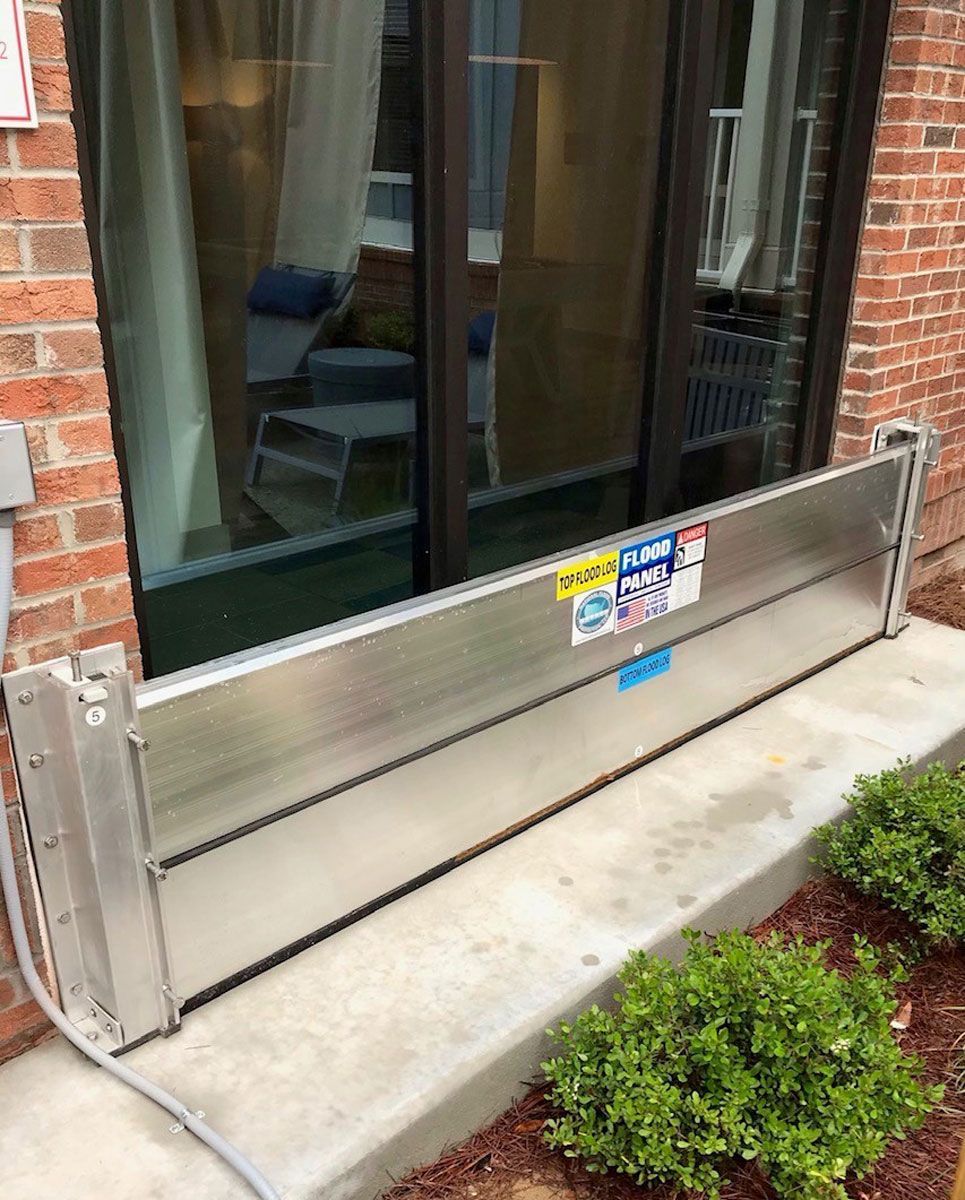A flood barrier is sitting on the sidewalk in front of a brick building.