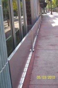 A sidewalk with a metal barrier along the side of a building.