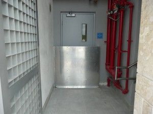 A hallway with a stainless steel door and red pipes.