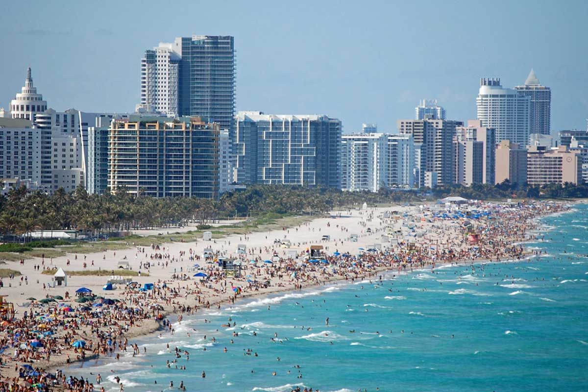 A crowded beach with a city skyline in the background.