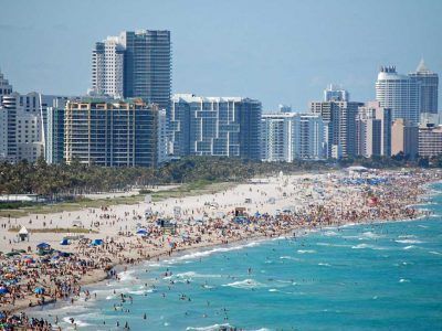 A crowded beach with a city in the background.