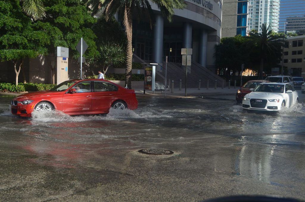 A red car is driving through a flooded street.