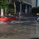 A red car is driving through a flooded street.