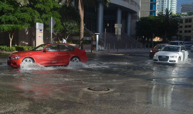 A red car is driving through a flooded street.