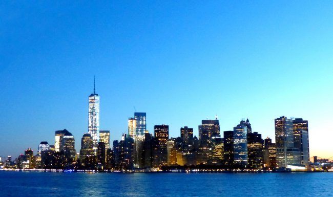 A city skyline with a blue sky and a body of water in the foreground