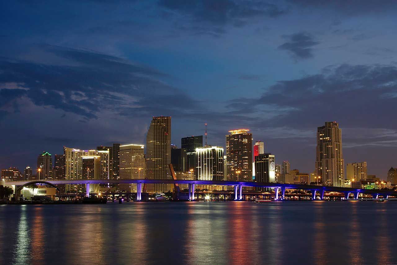 A city skyline at night with a bridge over a body of water.