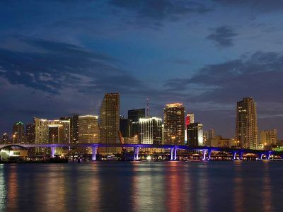 A city skyline at night with a bridge over a body of water.