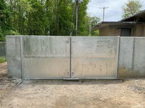 A large metal gate is sitting in the dirt in front of a house.