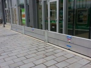 A brick sidewalk with a flood barrier in front of a building.