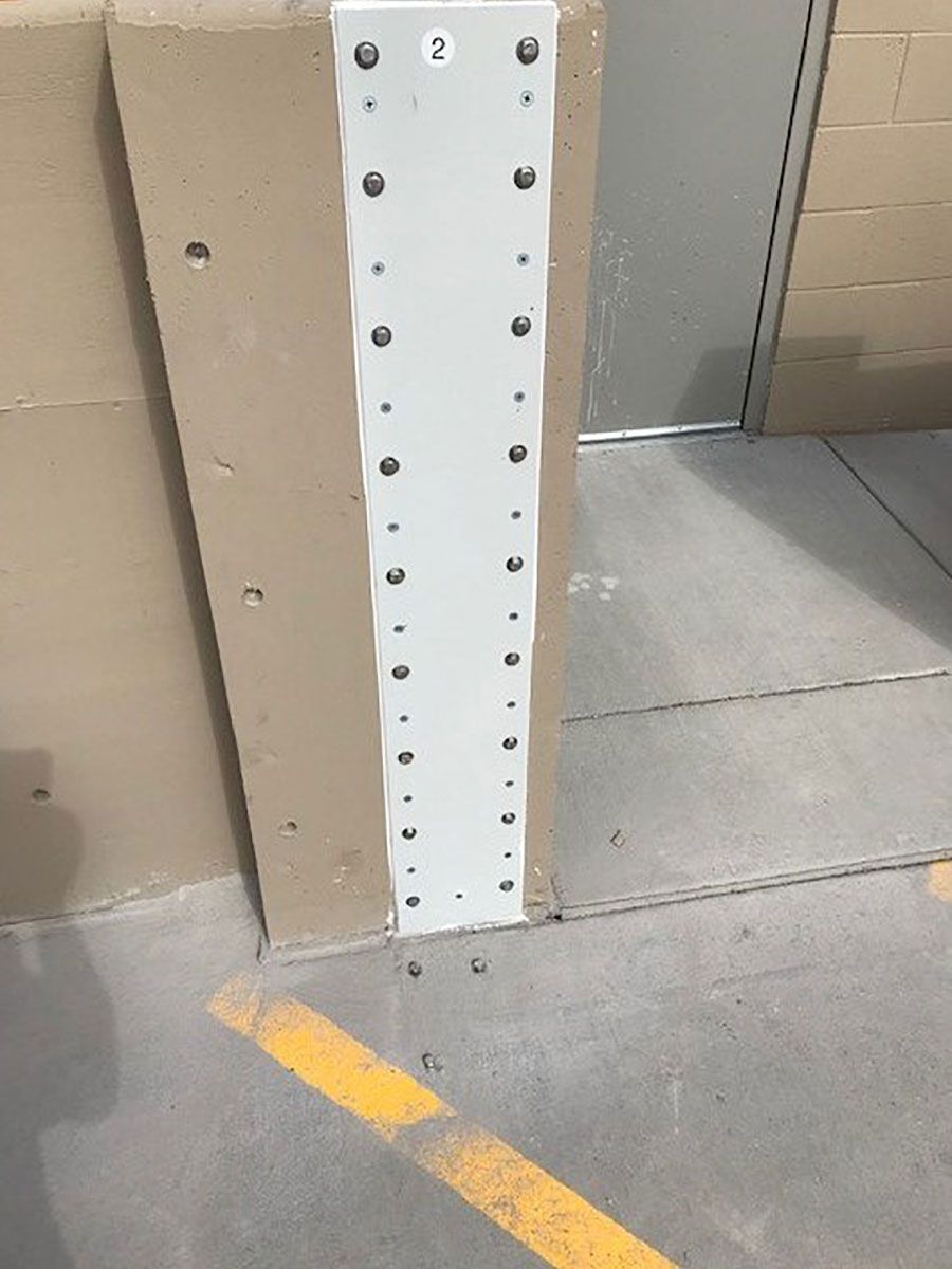 A white pole with holes in it is sitting on a sidewalk next to a door.