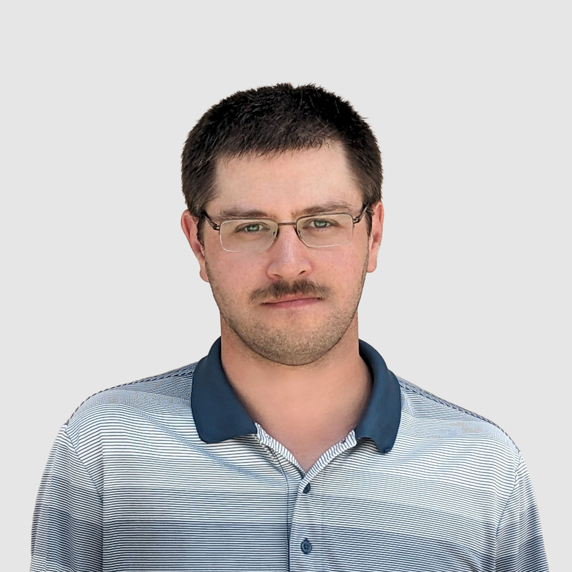 A man wearing glasses and a striped shirt is standing in front of a white background.