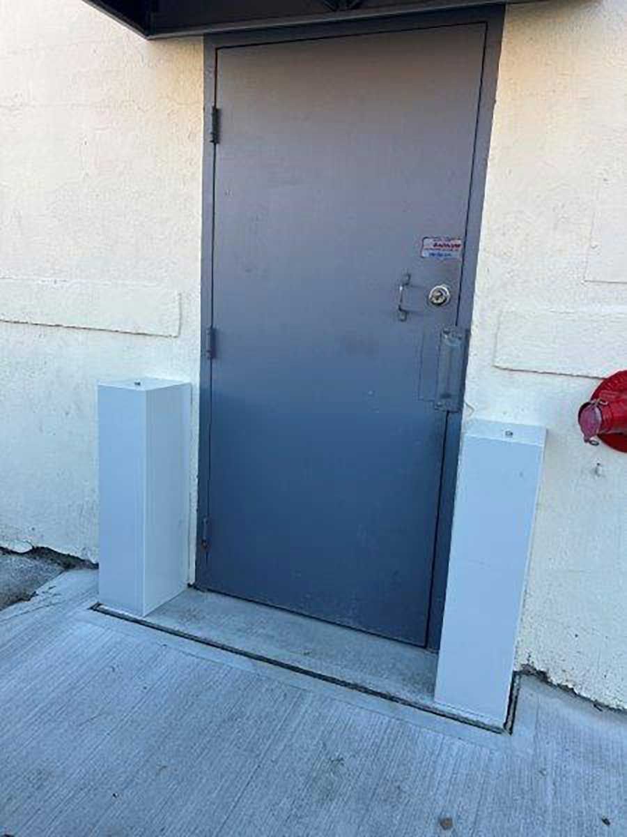 A gray door is sitting on the side of a building next to a fire hydrant.