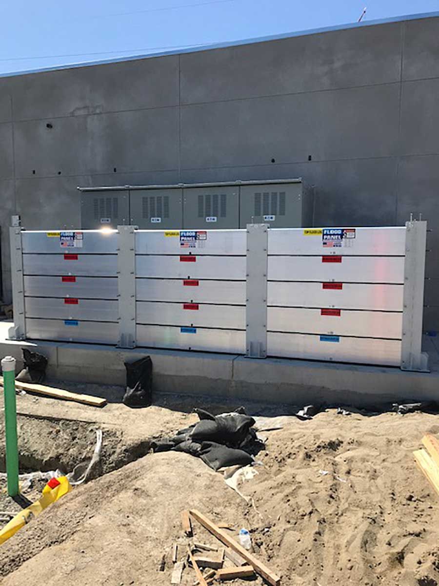 A row of aluminum flood barriers are sitting in front of a building under construction.