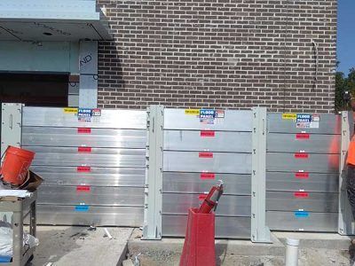 A man is standing in front of a brick building with flood barriers.