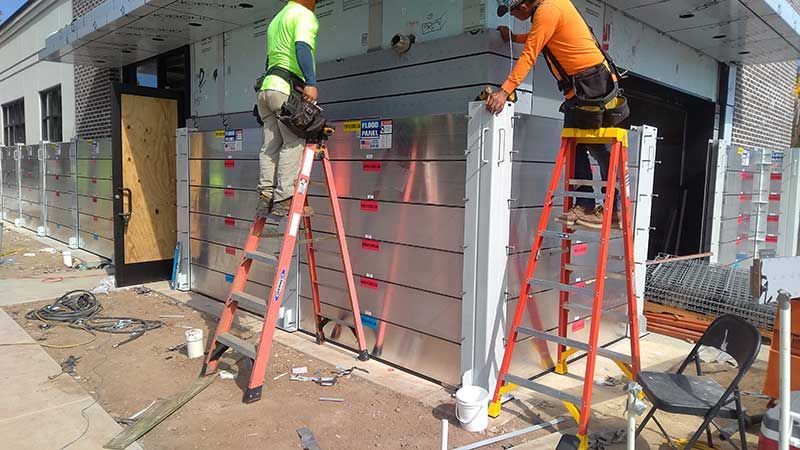 Two men are standing on ladders working on a wall.