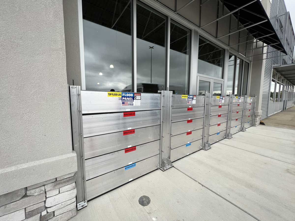 A row of aluminum flood barriers on the sidewalk in front of a building.