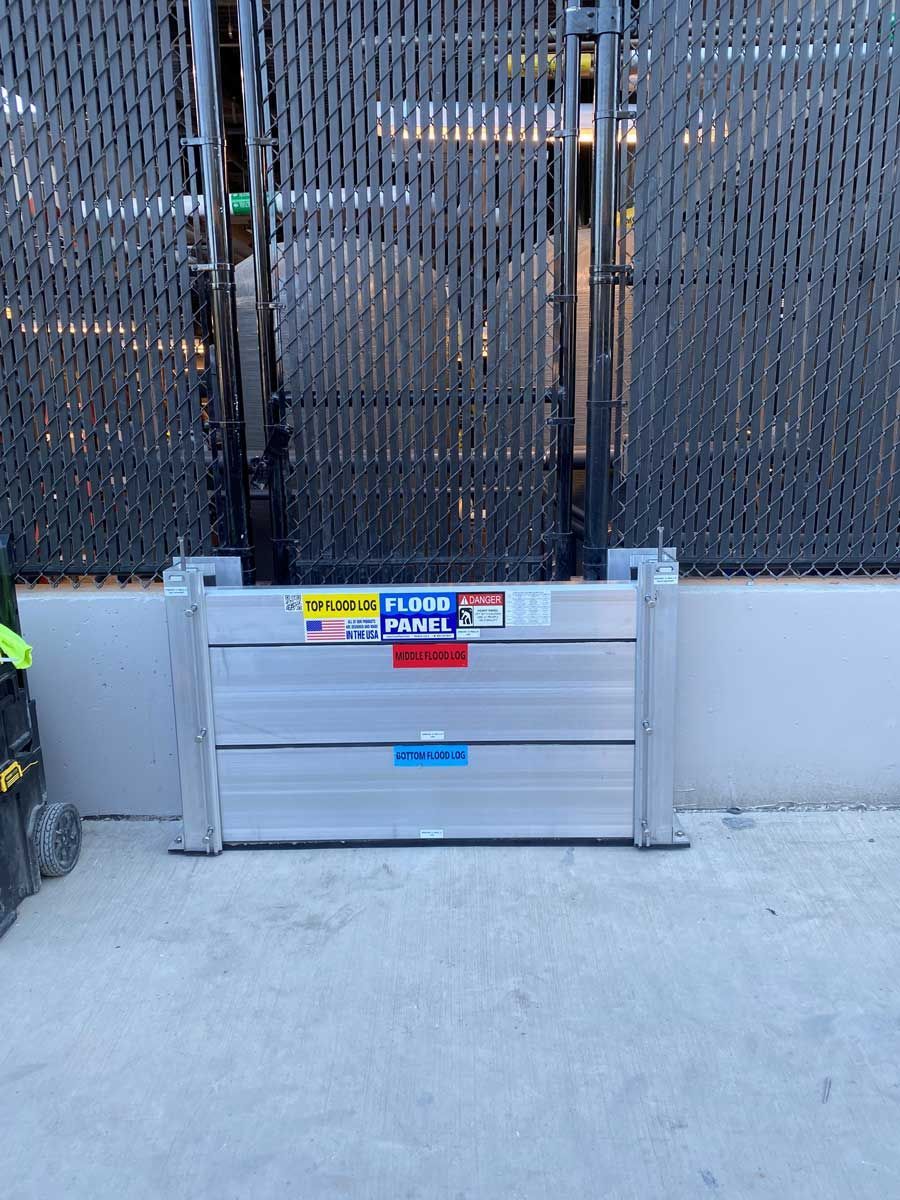 A flood barrier is sitting on the ground in front of a fence.