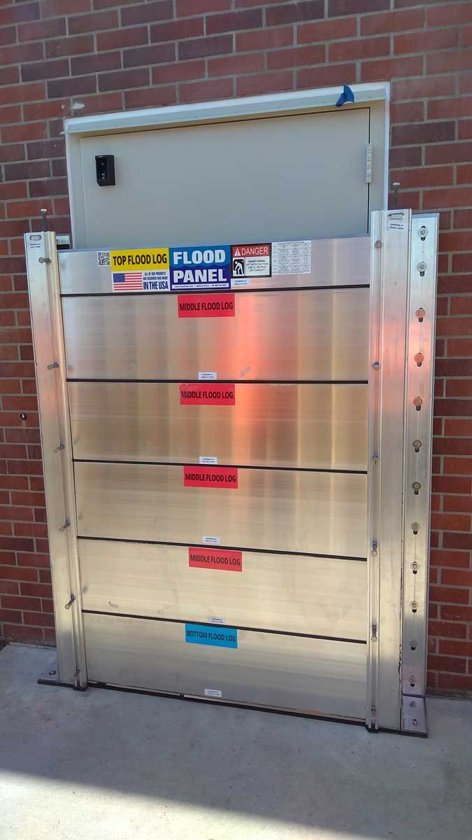 A stainless steel flood barrier is sitting in front of a brick wall