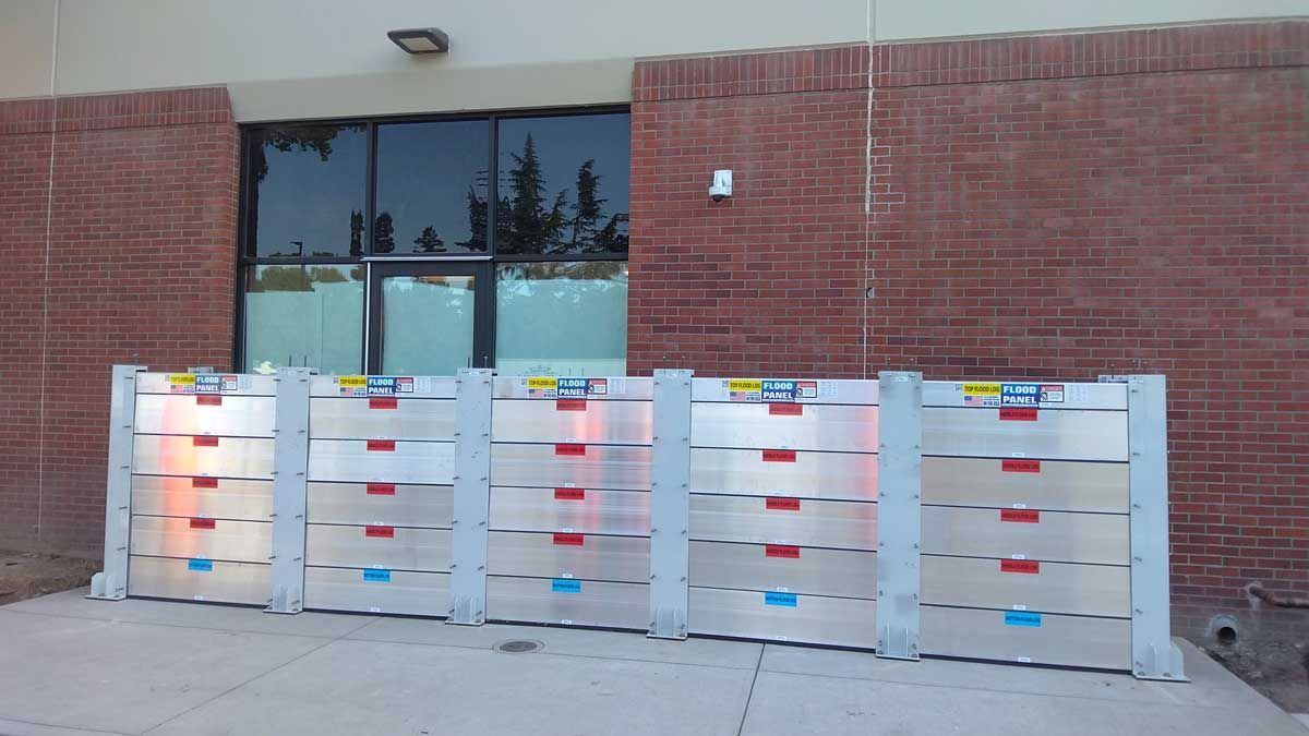 A row of flood barriers are lined up in front of a brick building.
