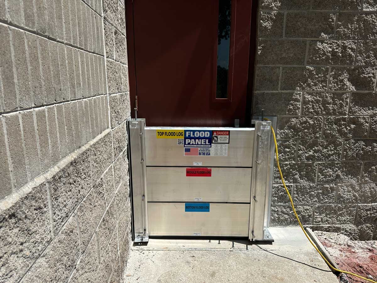 A flood gate is attached to a brick wall next to a door.