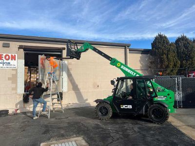 A man is standing on a ladder next to a forklift in front of a building.