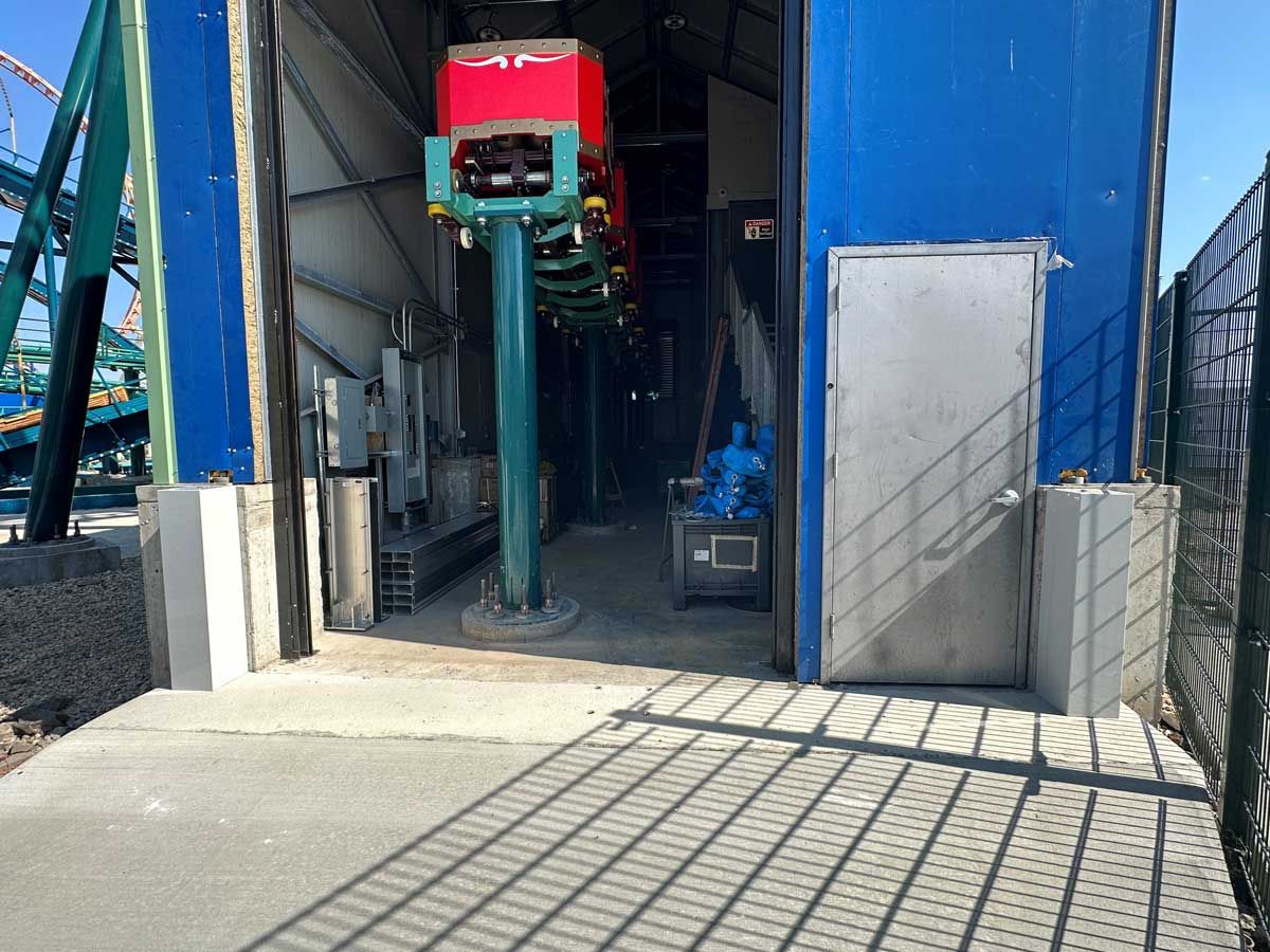 A roller coaster is sitting inside of a building with its doors open.
