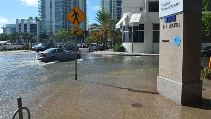 A car is driving through a flooded street in front of a building.