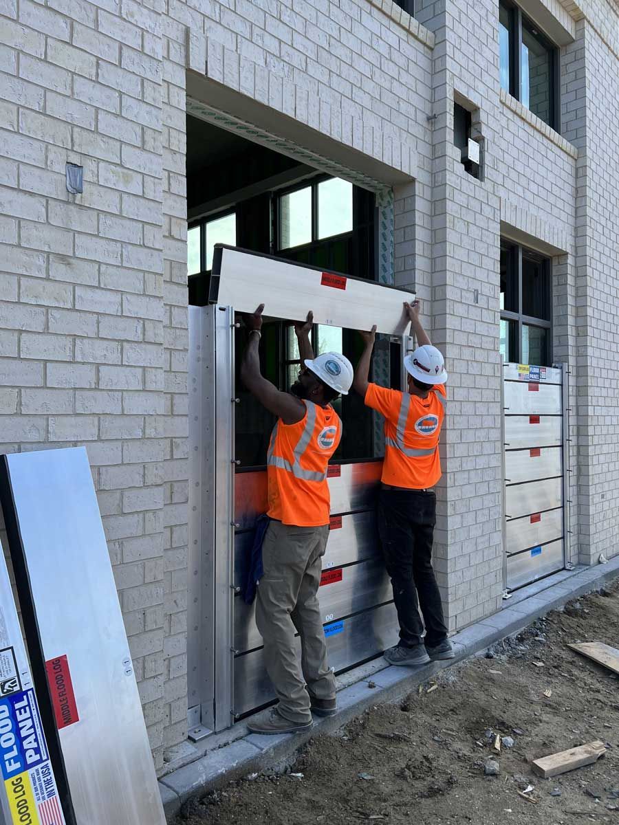 Two construction workers are installing a flood barrier on the side of a building.