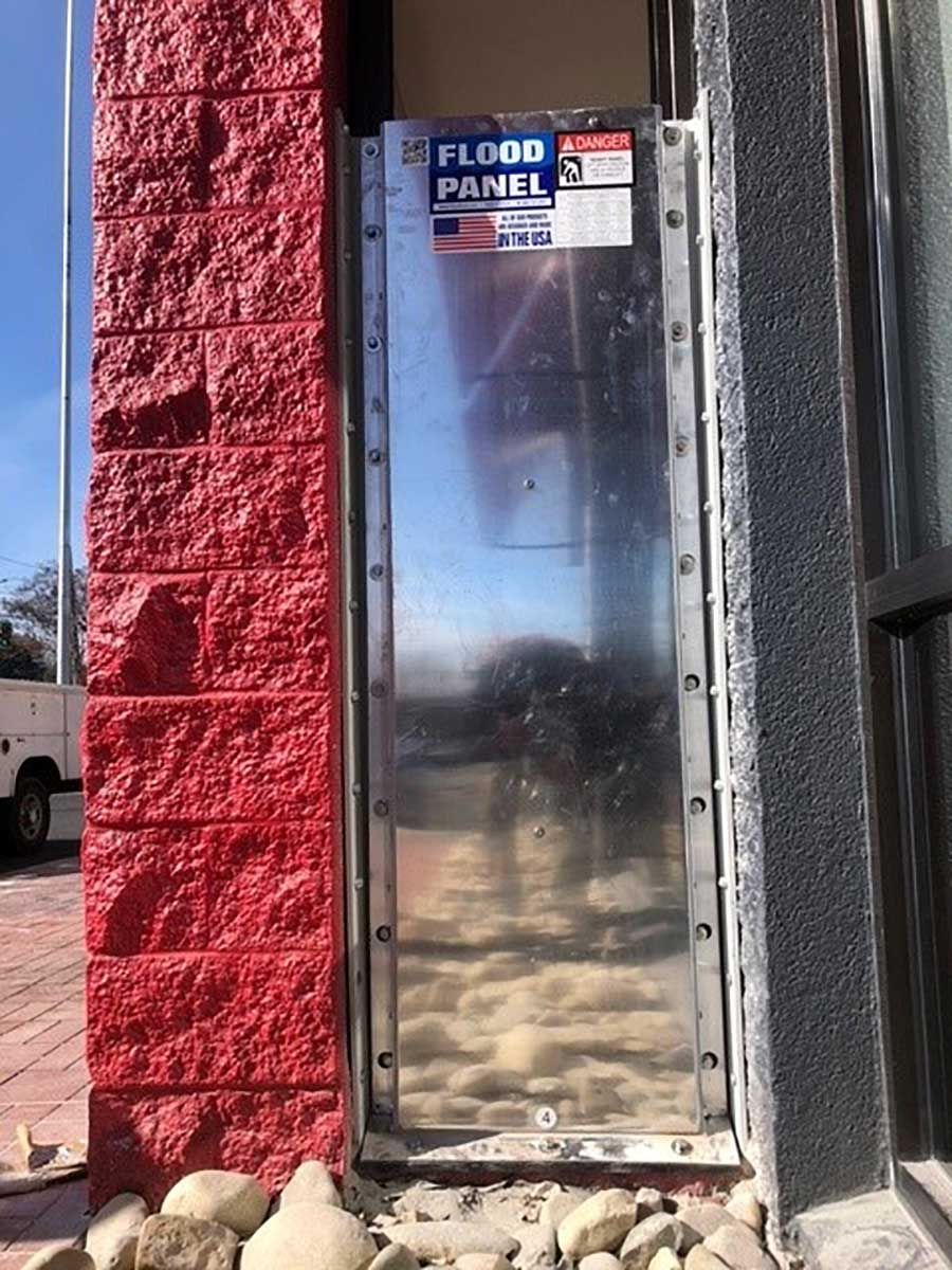 A flood panel is sitting on the side of a building next to a red brick wall.