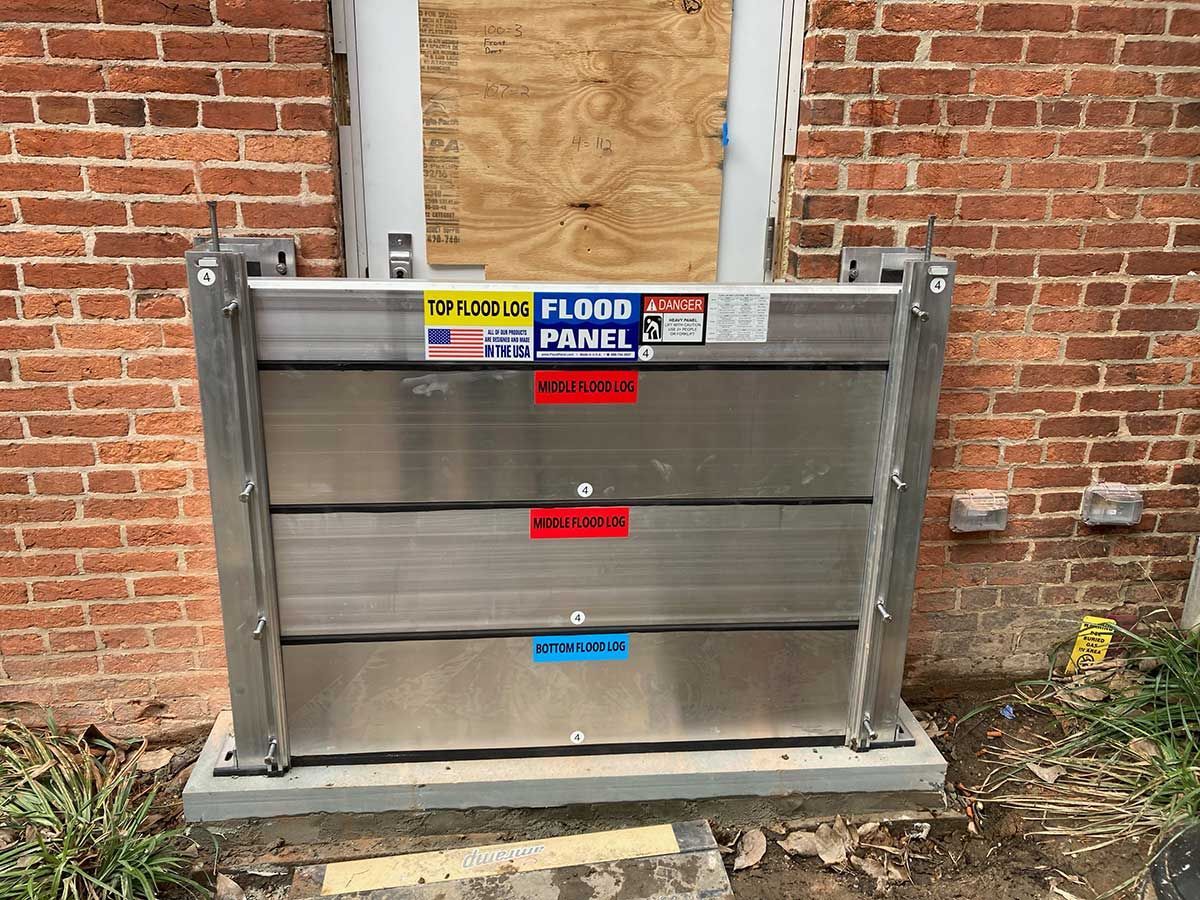 A stainless steel flood barrier is sitting in front of a brick building.