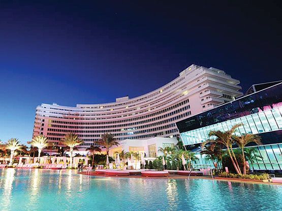 A large hotel with a swimming pool in front of it at night.