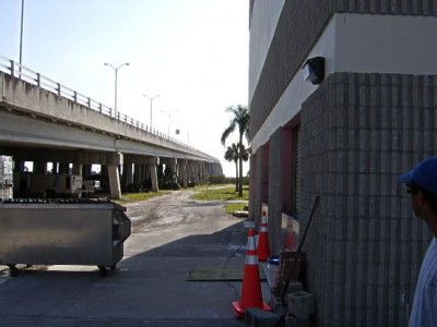 A man is standing in front of a building with a bridge in the background