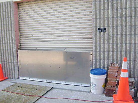 A white bucket with a blue lid sits next to two orange cones.