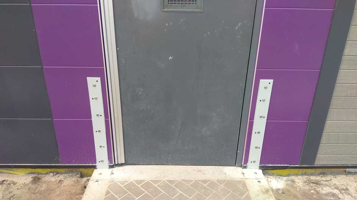 A door with a purple wall behind it and a brick walkway leading to it.