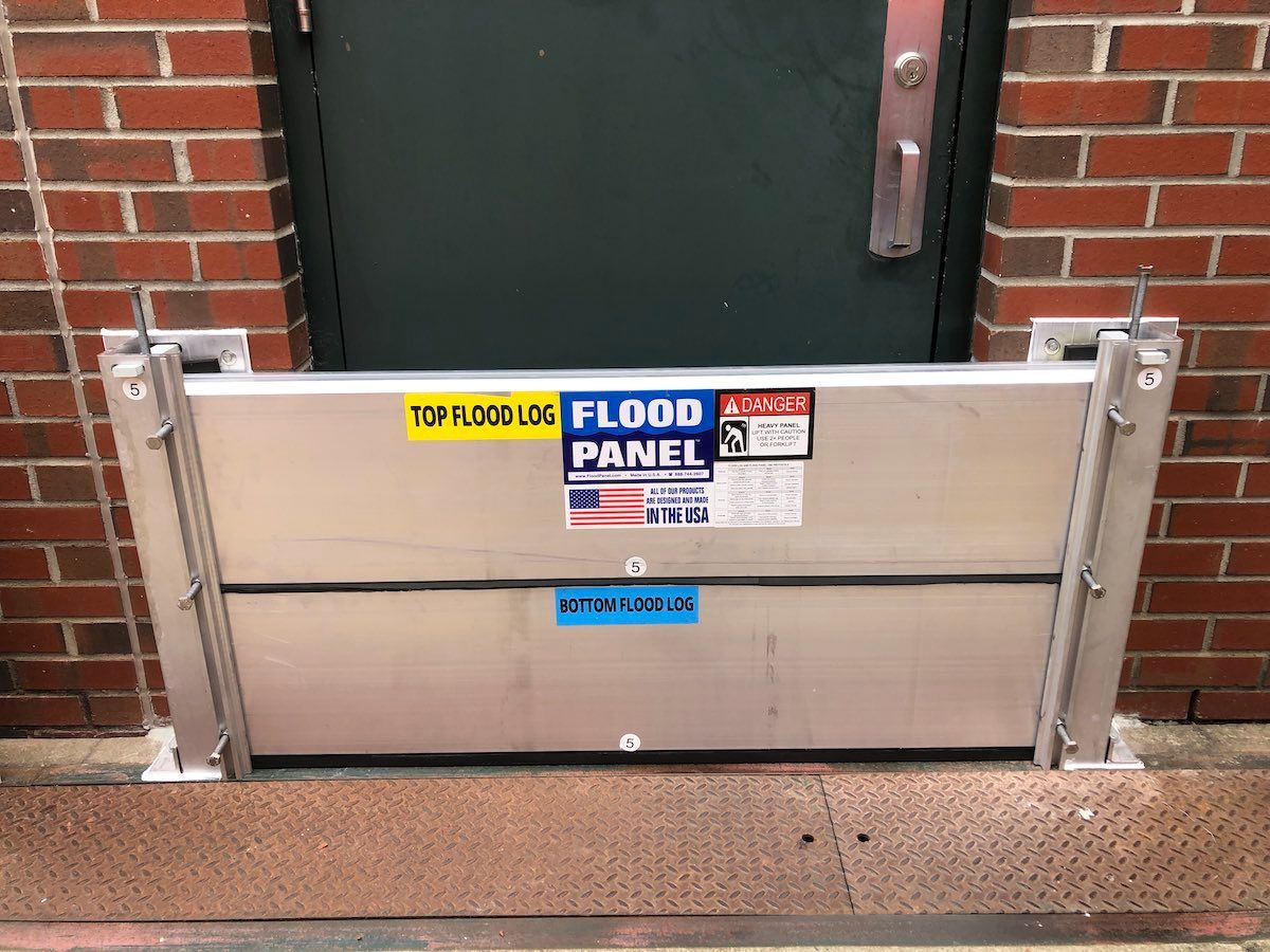 A flood panel is sitting in front of a door on a brick wall.