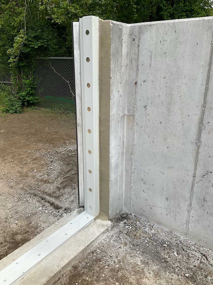 A close up of a concrete wall with a fence in the background.