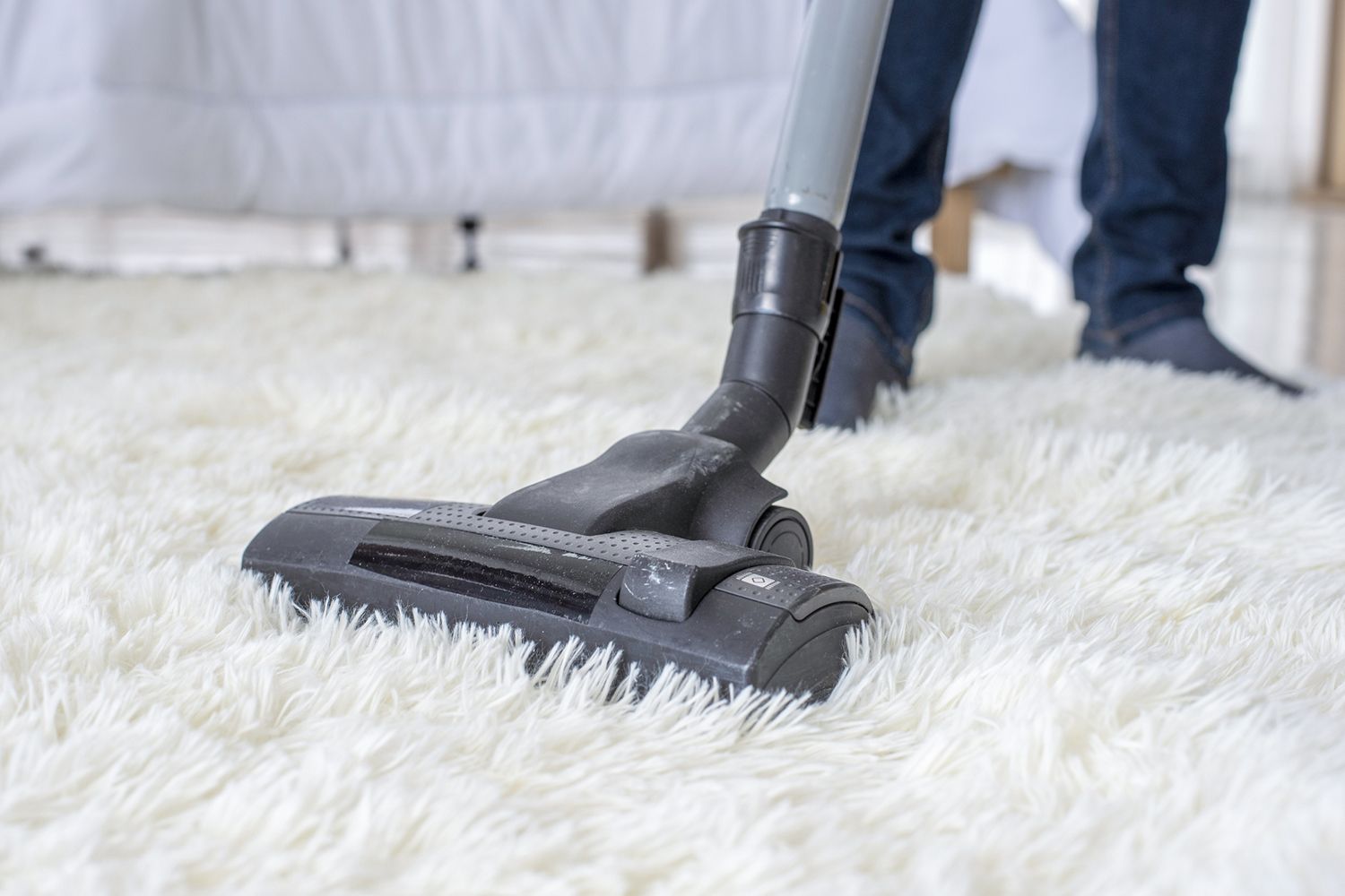 Person vacuuming a white, shaggy rug with a gray vacuum cleaner.