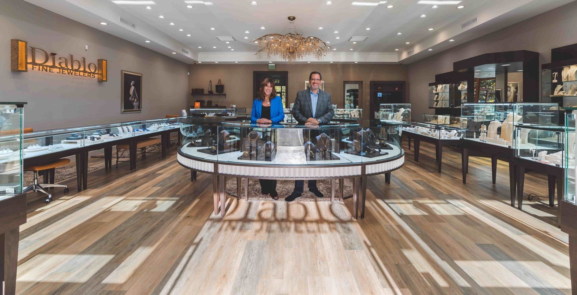 A jewelry store interior with two people standing behind a display case. There are glass displays on the sides with jewelry and watches.