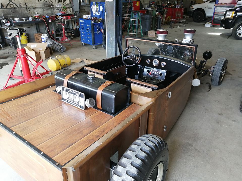 A wooden car is sitting in a garage next to a truck.