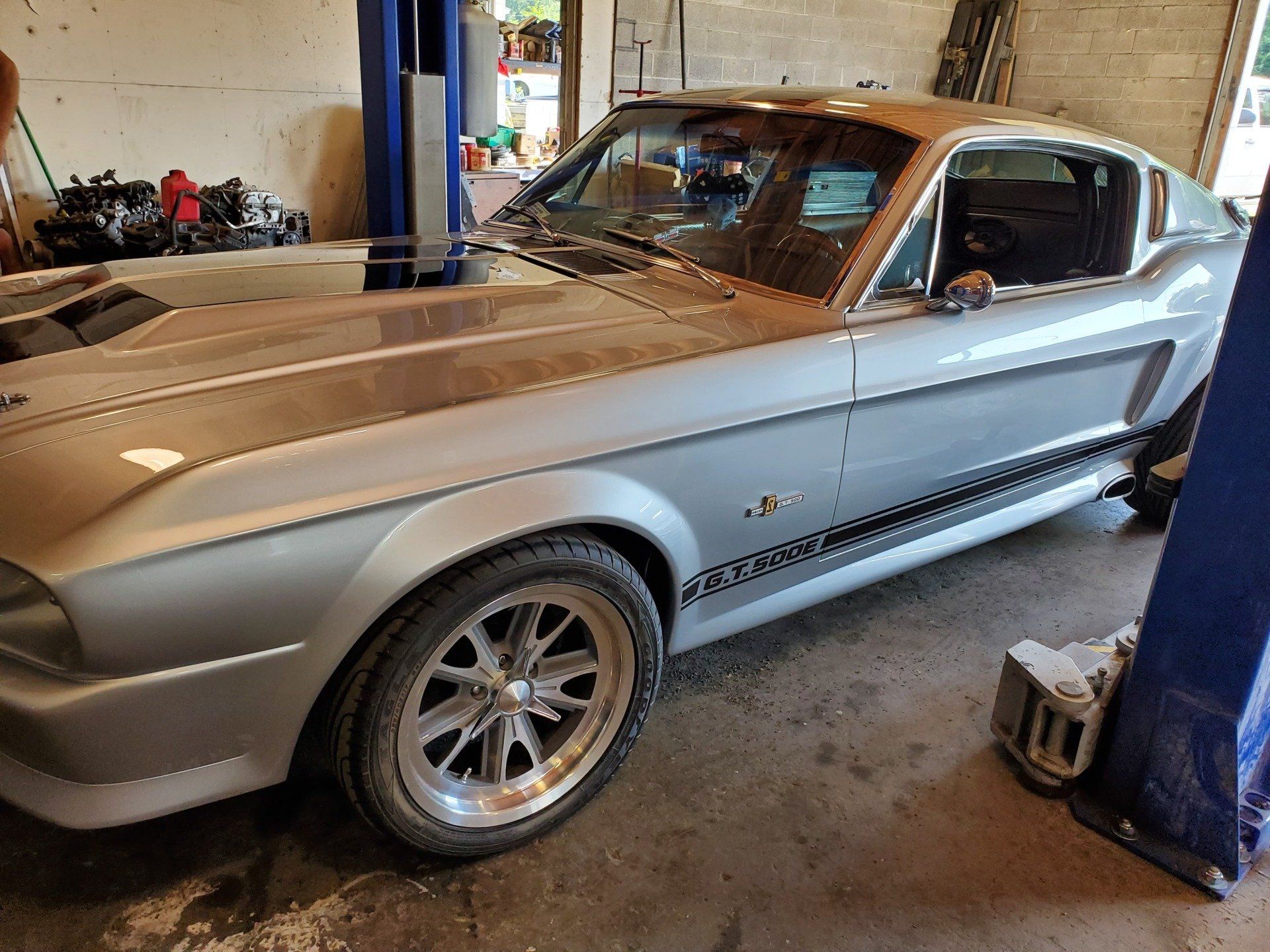 A silver mustang is parked in a garage on a lift.