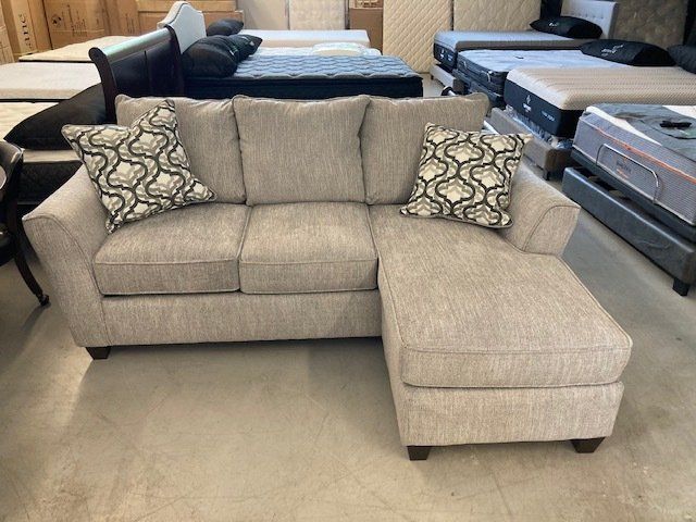 A sectional couch is sitting in a room with mattresses.