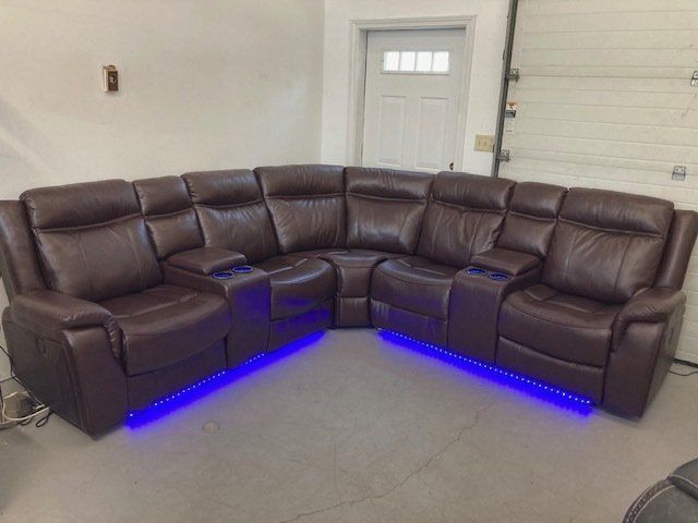 A brown leather sectional couch with blue lights underneath it in a living room.