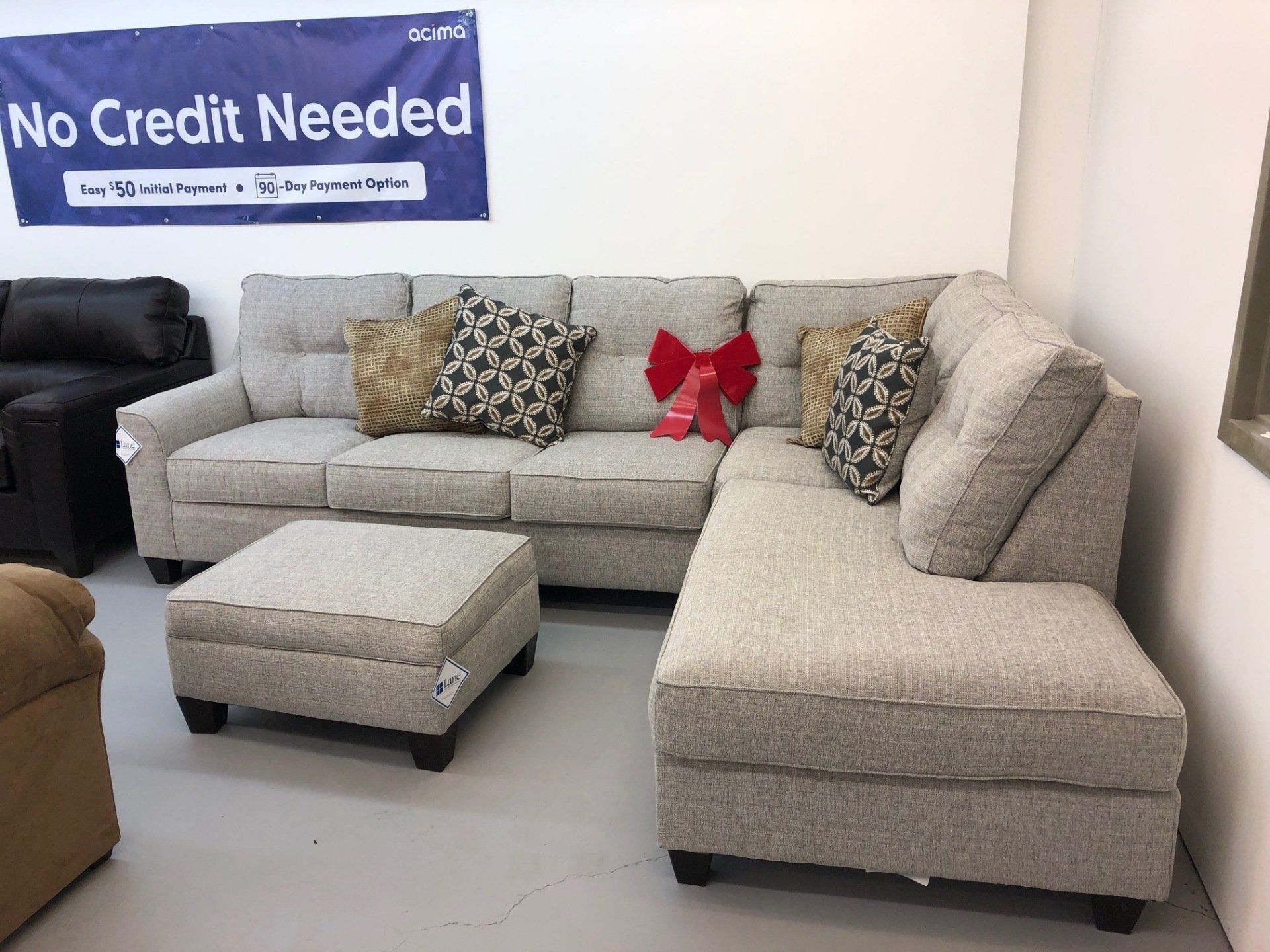 A sectional couch and ottoman in a living room with a sign that says no credit needed.