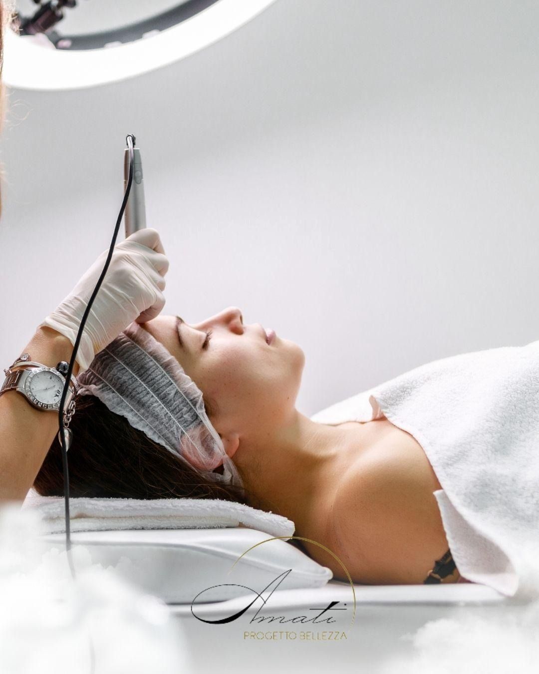 Un'estetista professionista utilizza un dispositivo medico portatile per eseguire un trattamento viso su una cliente sdraiata su un lettino da spa.