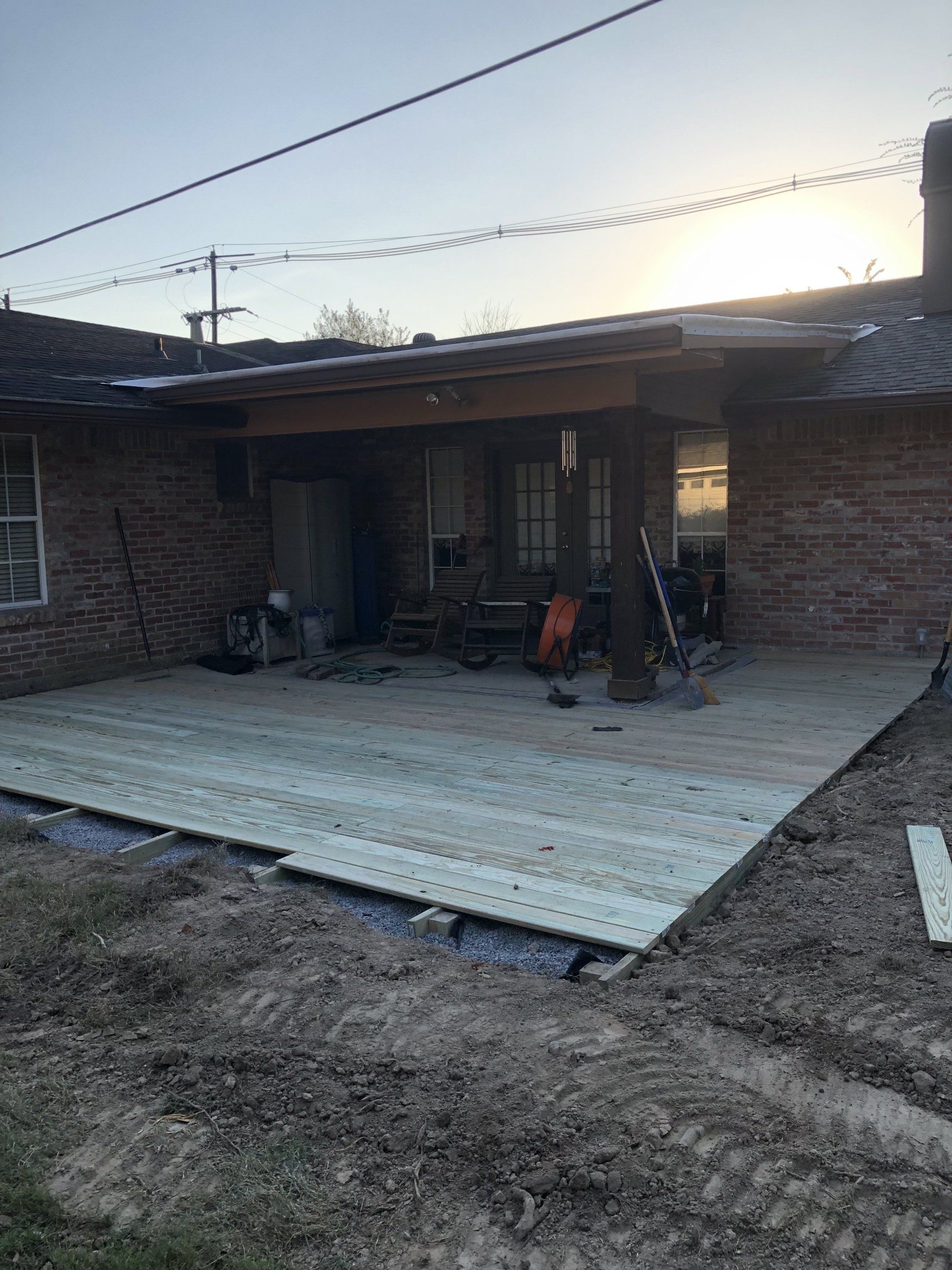 A new wooden deck being built outside a brick house. The deck is partially constructed on a gravel base.