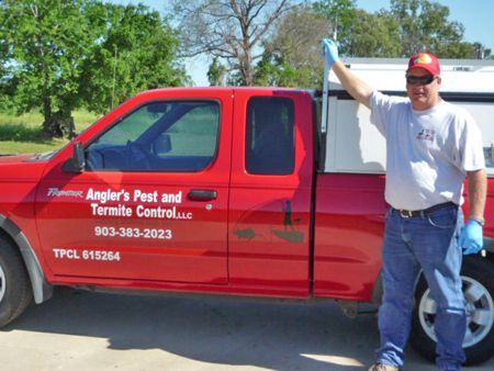 A man standing in front of a red truck that says angler 's pest and termite control