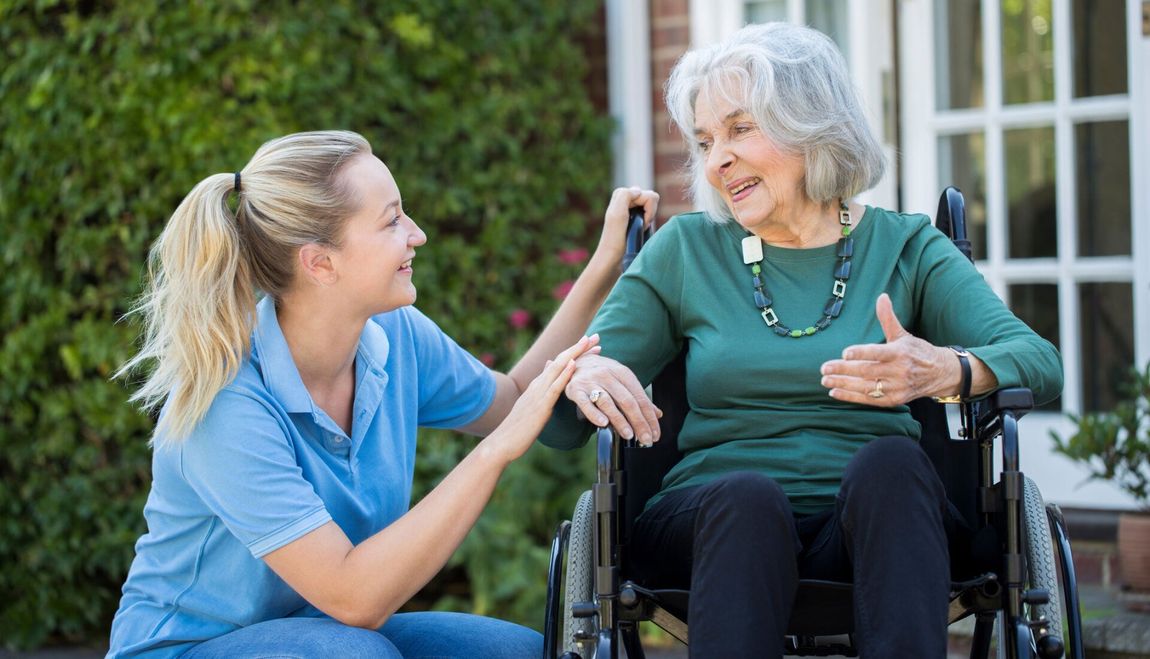 Carer Pushing Senior Woman In Wheelchair Outside Home